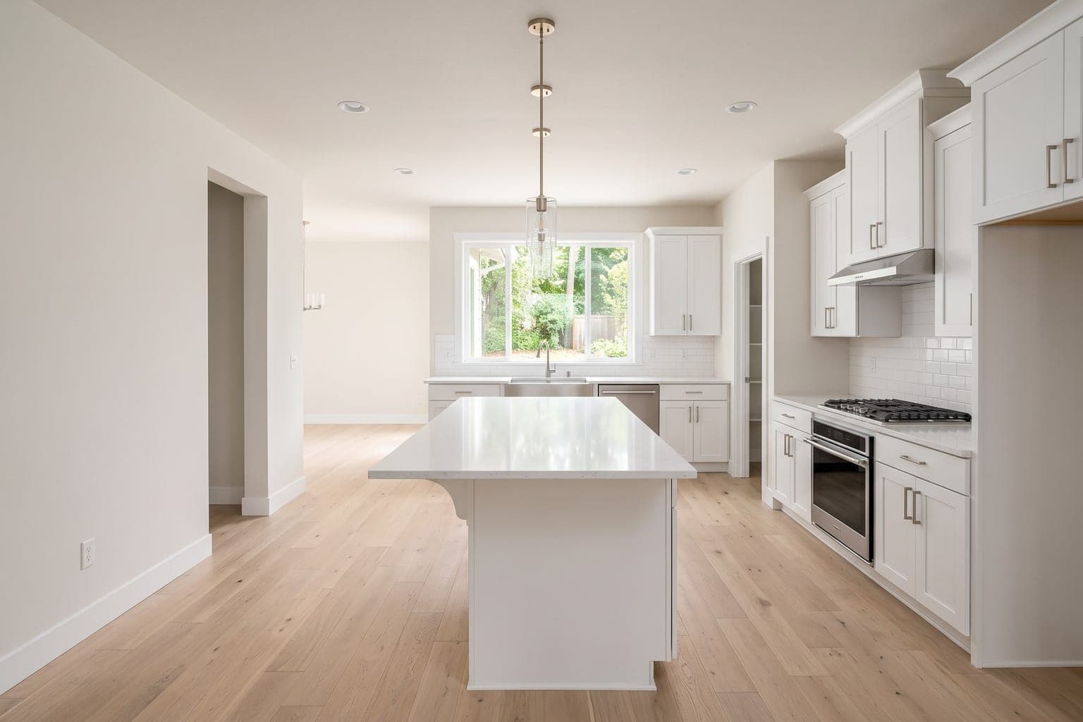 Empty white kitchen with an island before virtual staging - light oak floor, white cabinets, bare counters